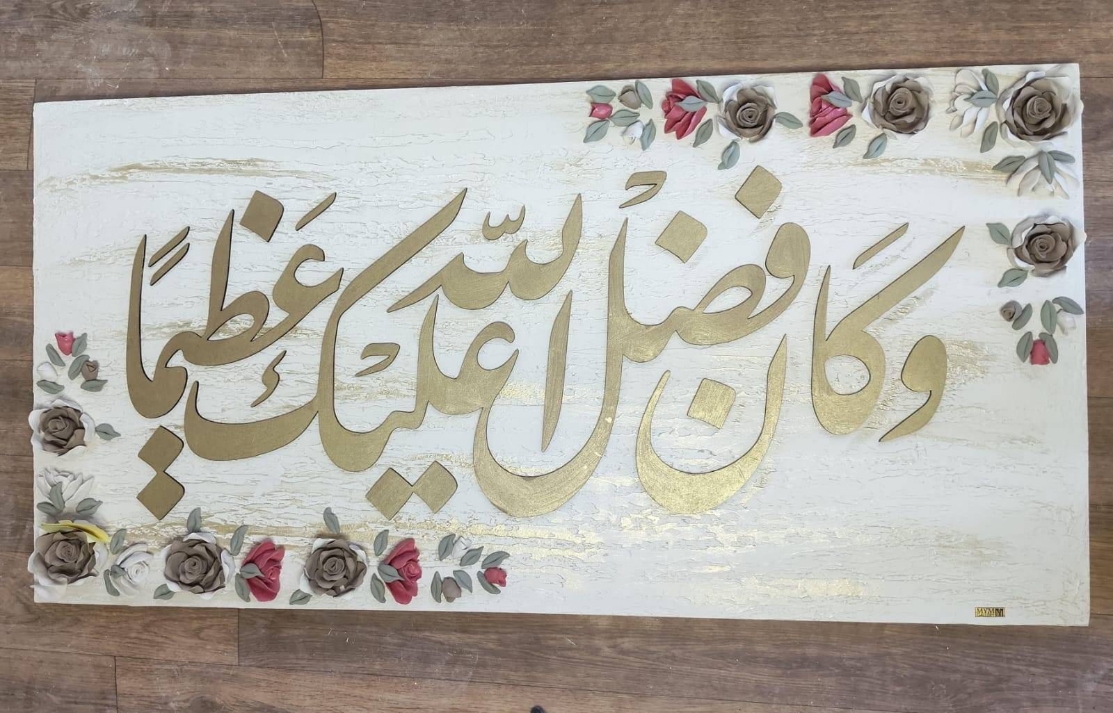 Gilded Arabic calligraphy on a white board with roses in two corners